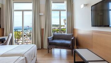 A hotel room with a bed, a sofa, a TV, and a balcony with a view of the sea.
