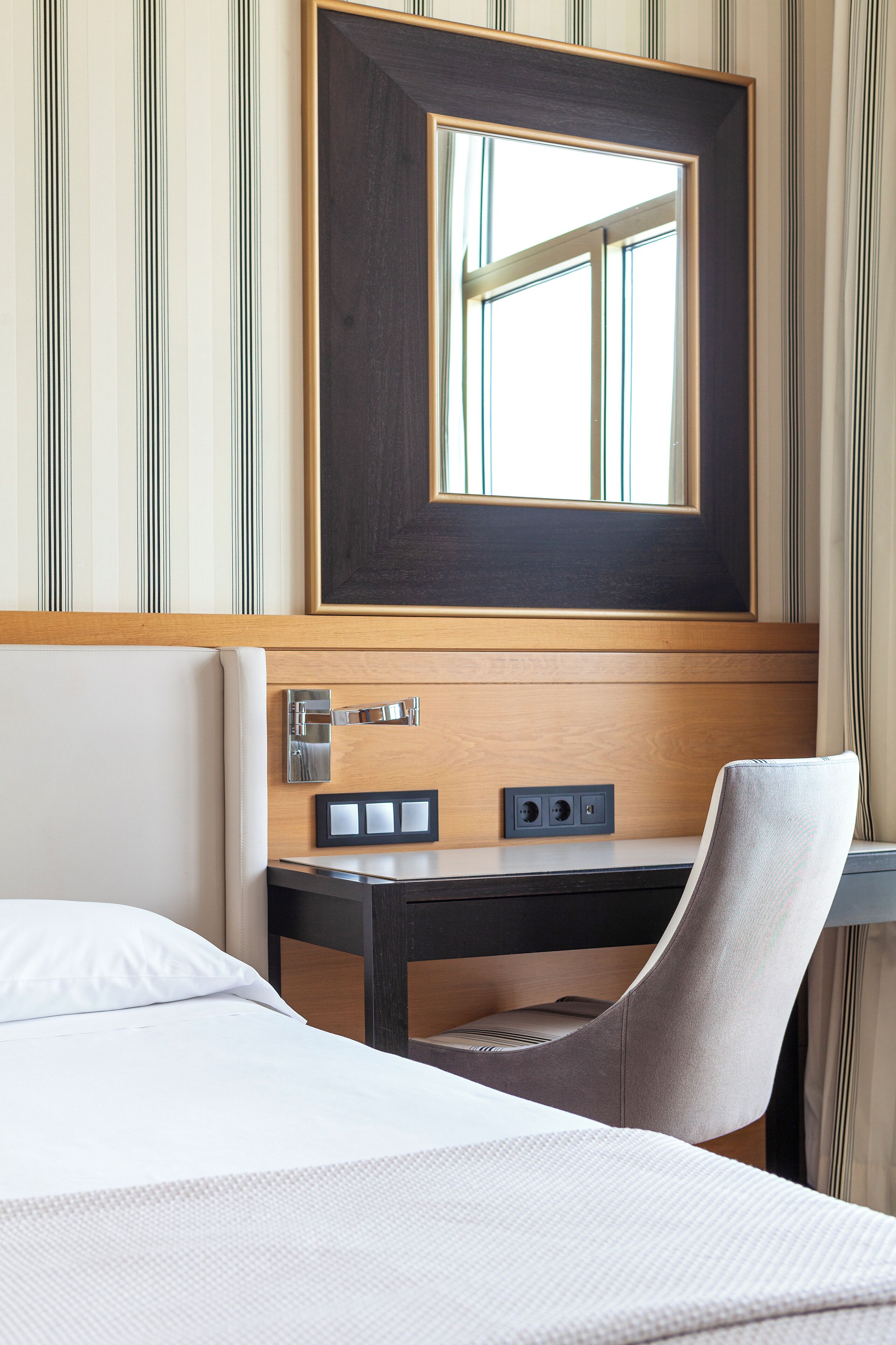 A hotel room with a bed, a desk, a chair, a mirror, and a window.