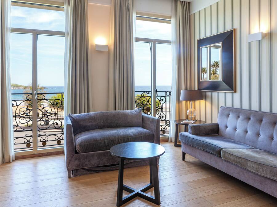 A living room with a sofa, a round table, and a view of the sea through large windows.