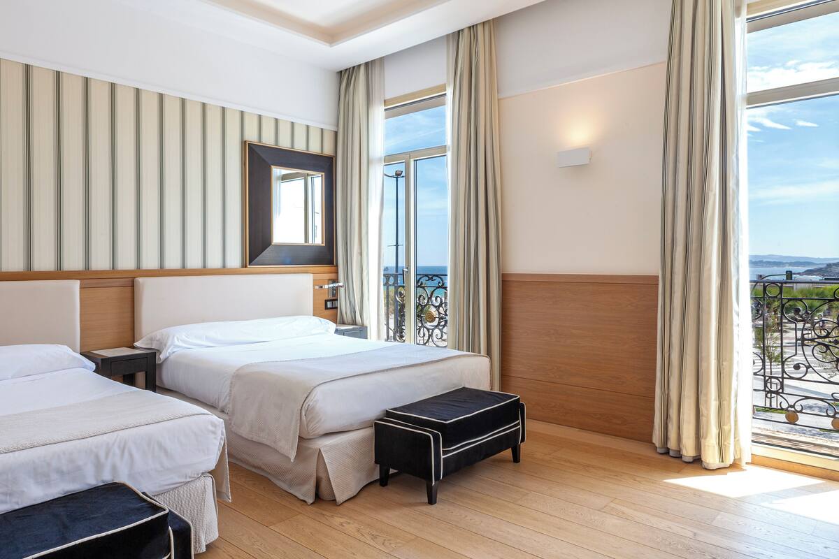 A hotel room with two beds, a large window with a view, a wooden headboard, and a small table.