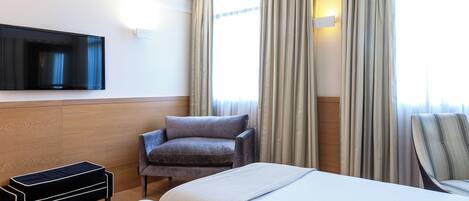 A hotel room with a bed, a chair, a TV, and curtains.