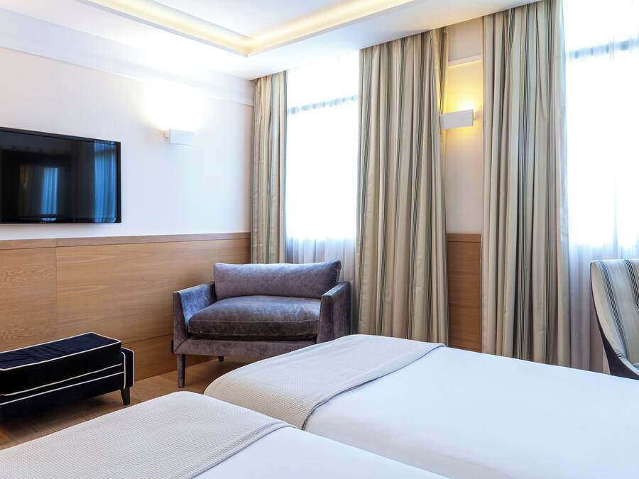 A hotel room with a bed, a chair, a TV, and curtains.