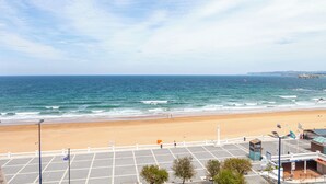 A beach view with a parking lot, a building with a sign, and a flagpole. - Gran Hotel Sardinero (Santander)