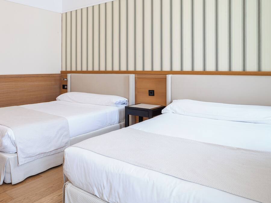A hotel room with two single beds, a wooden headboard, a striped wall, and a small bedside table.
