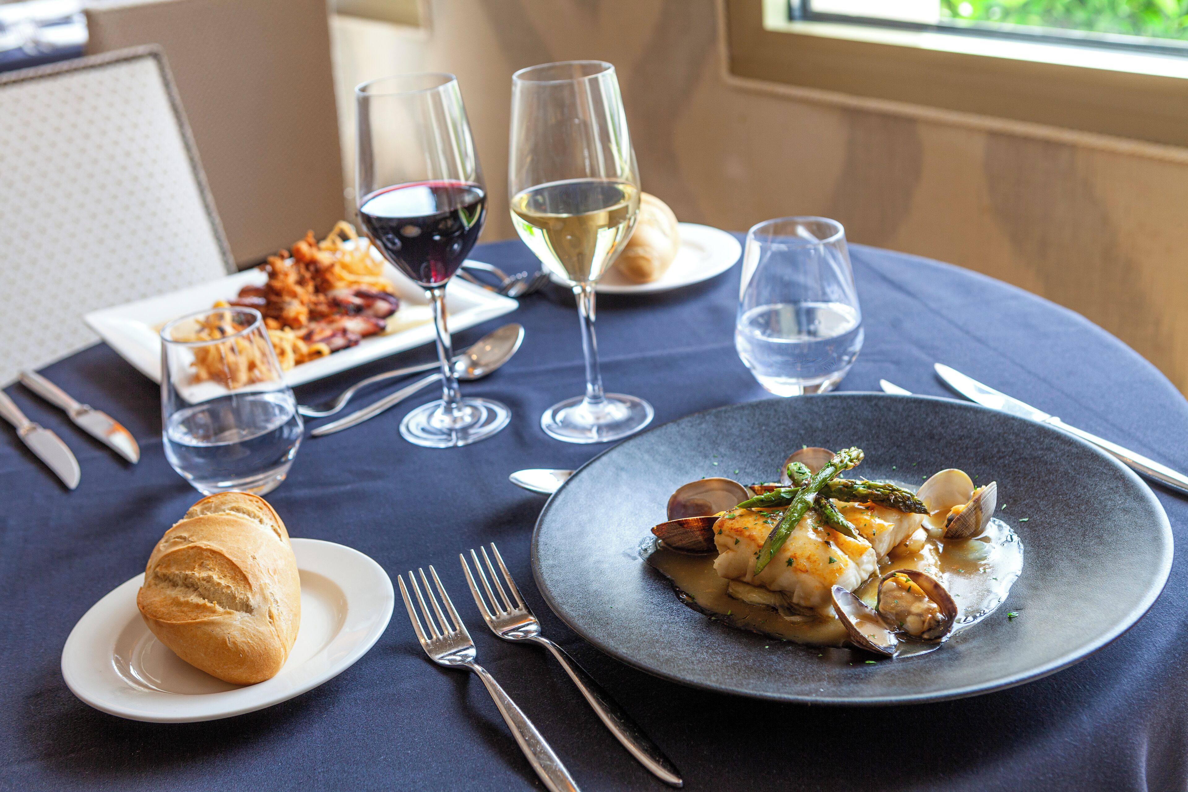 A dining table with plates of food, wine glasses, and cutlery.