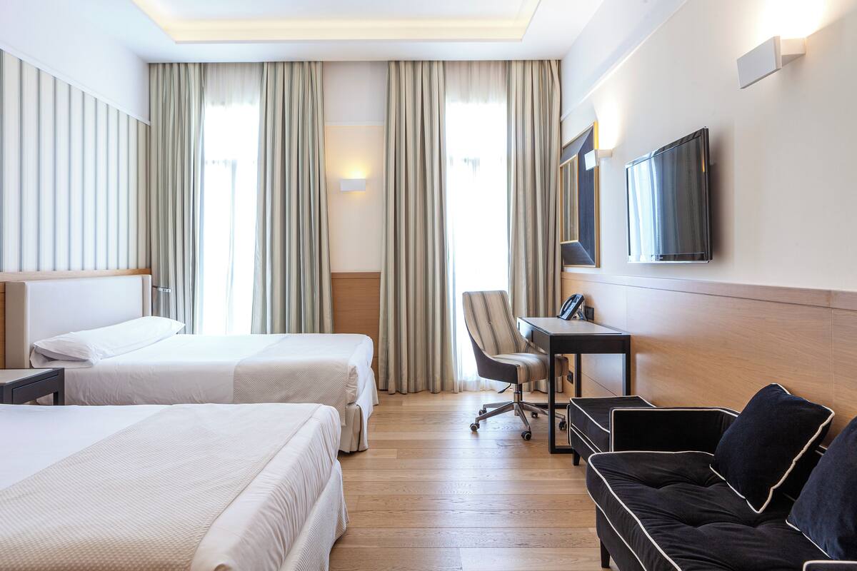 A hotel room with two beds, a desk, a chair, a sofa, and a TV.