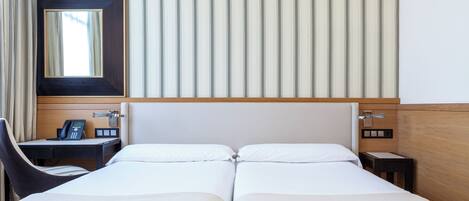 A hotel room with two beds, a desk with a phone, a chair, and a mirror.