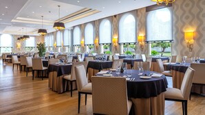 A spacious dining area with multiple tables set for dining, large windows with arched tops, and modern chandeliers. - Gran Hotel Sardinero (Santander)