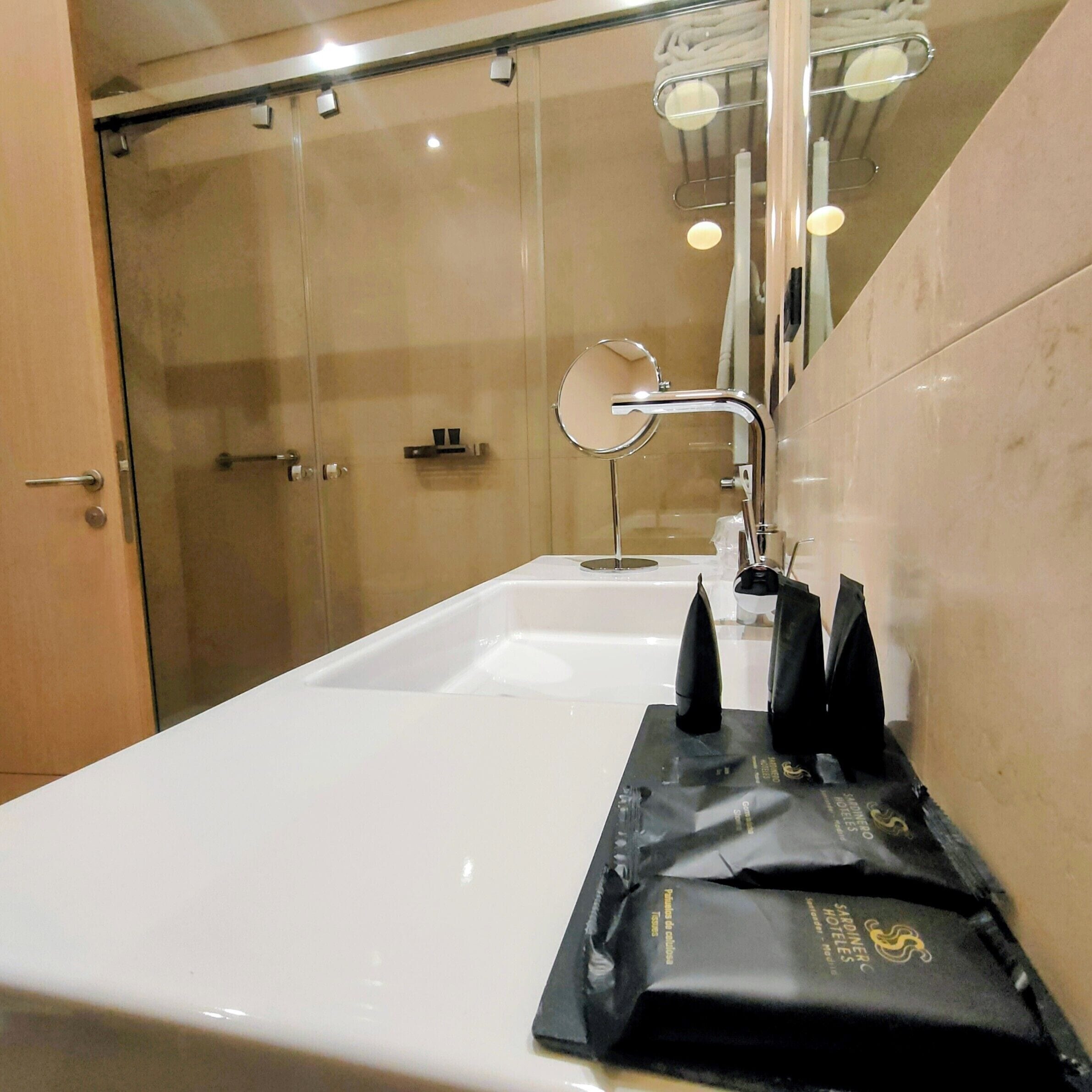 Un baño con lavamanos blanco, cabina de ducha de vidrio y toallero.