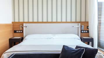 Habitación de hotel con una cama grande, cabecero de madera, dos mesitas de noche y un ventanal con cortinas.