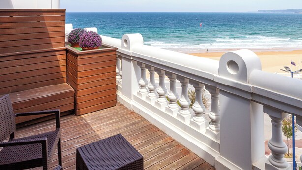 A balcony with wooden flooring, white balustrades, wicker furniture, and a view of the beach and ocean. - Gran Hotel Sardinero (Santander)