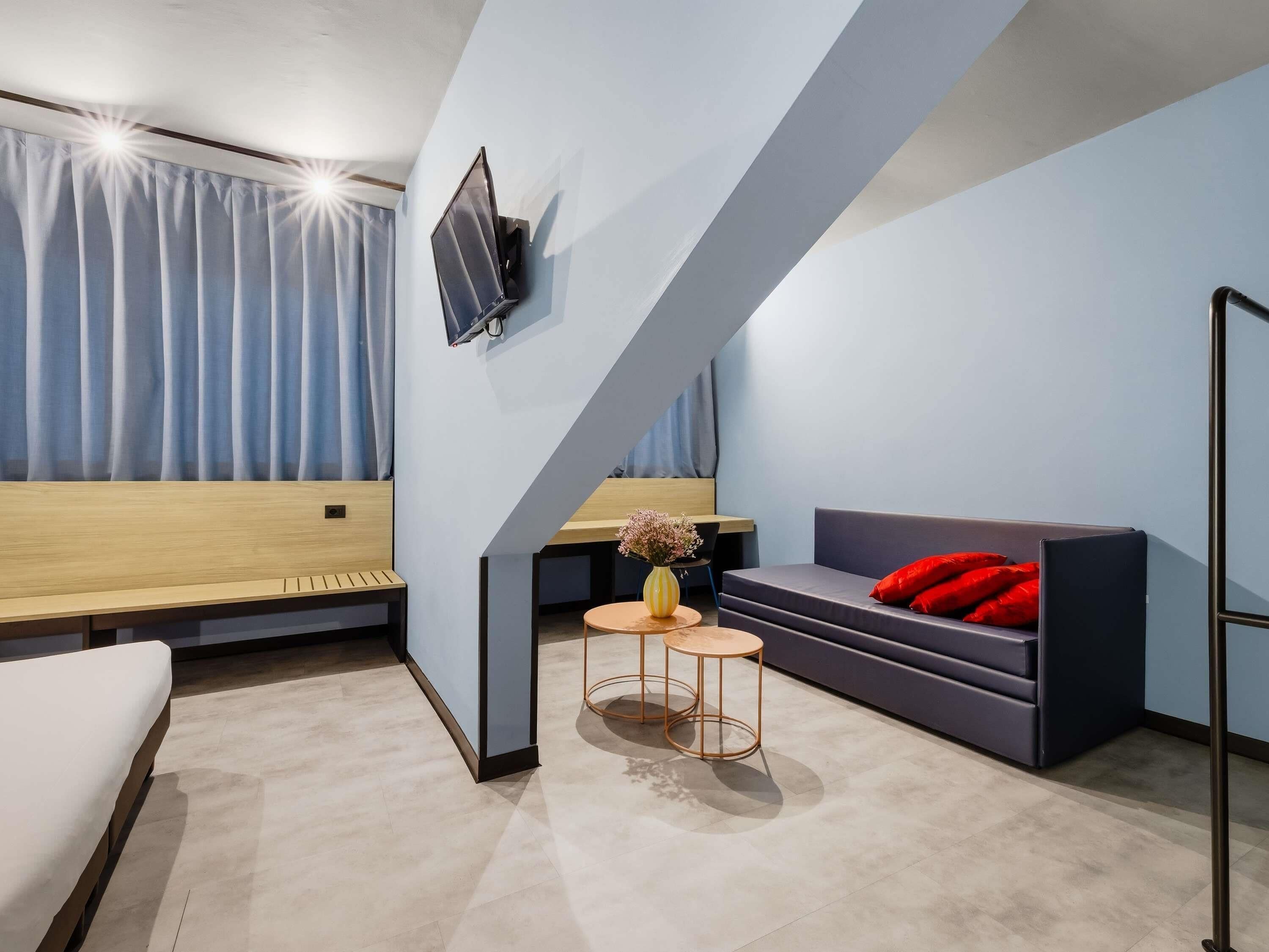 A modern room with a sofa, a small table with a vase, a bench, and a TV mounted on the wall.
