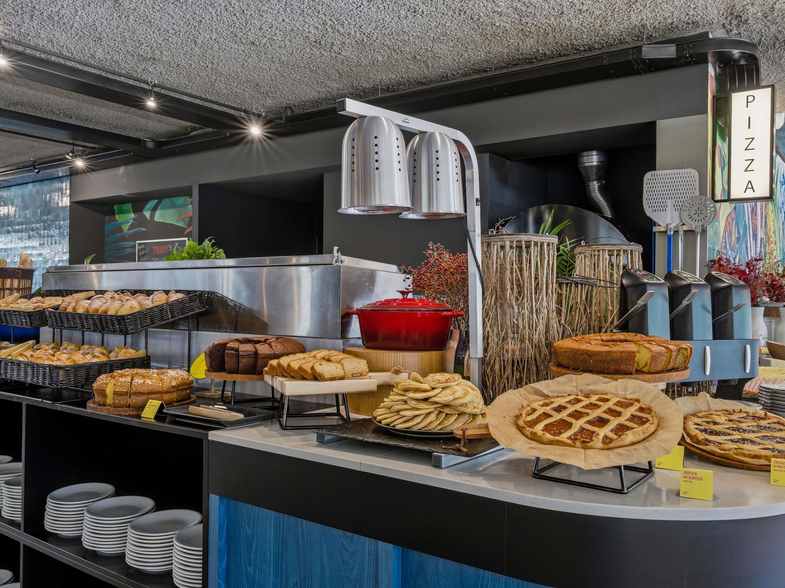 Mostrador de panadería con varios productos horneados, un letrero de pizza y una exhibición de platos.