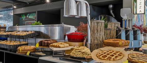 Mostrador de panadería con varios productos horneados, un letrero de pizza y una exhibición de platos.