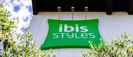 En grön skylt med texten ”ibis Styles” på en byggnads fasad.