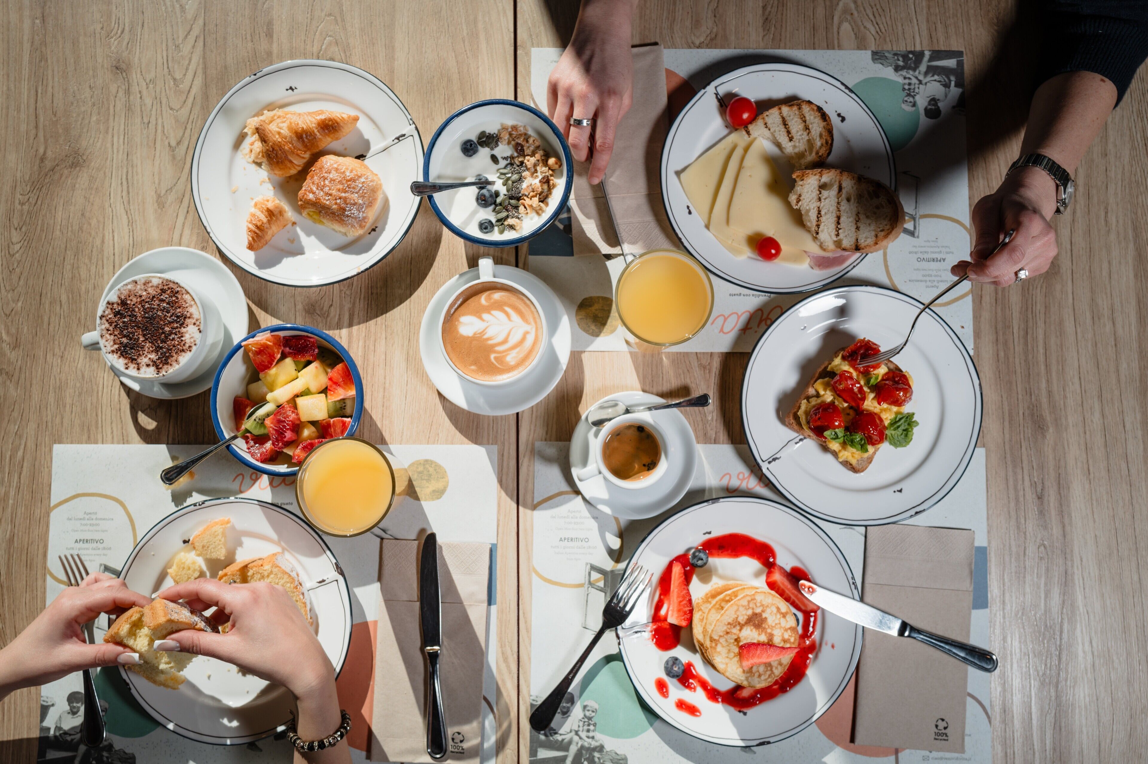 Una mesa con diversos productos de desayuno, como pasteles, frutas y bebidas, dispuesta sobre una mesa de madera con menús.