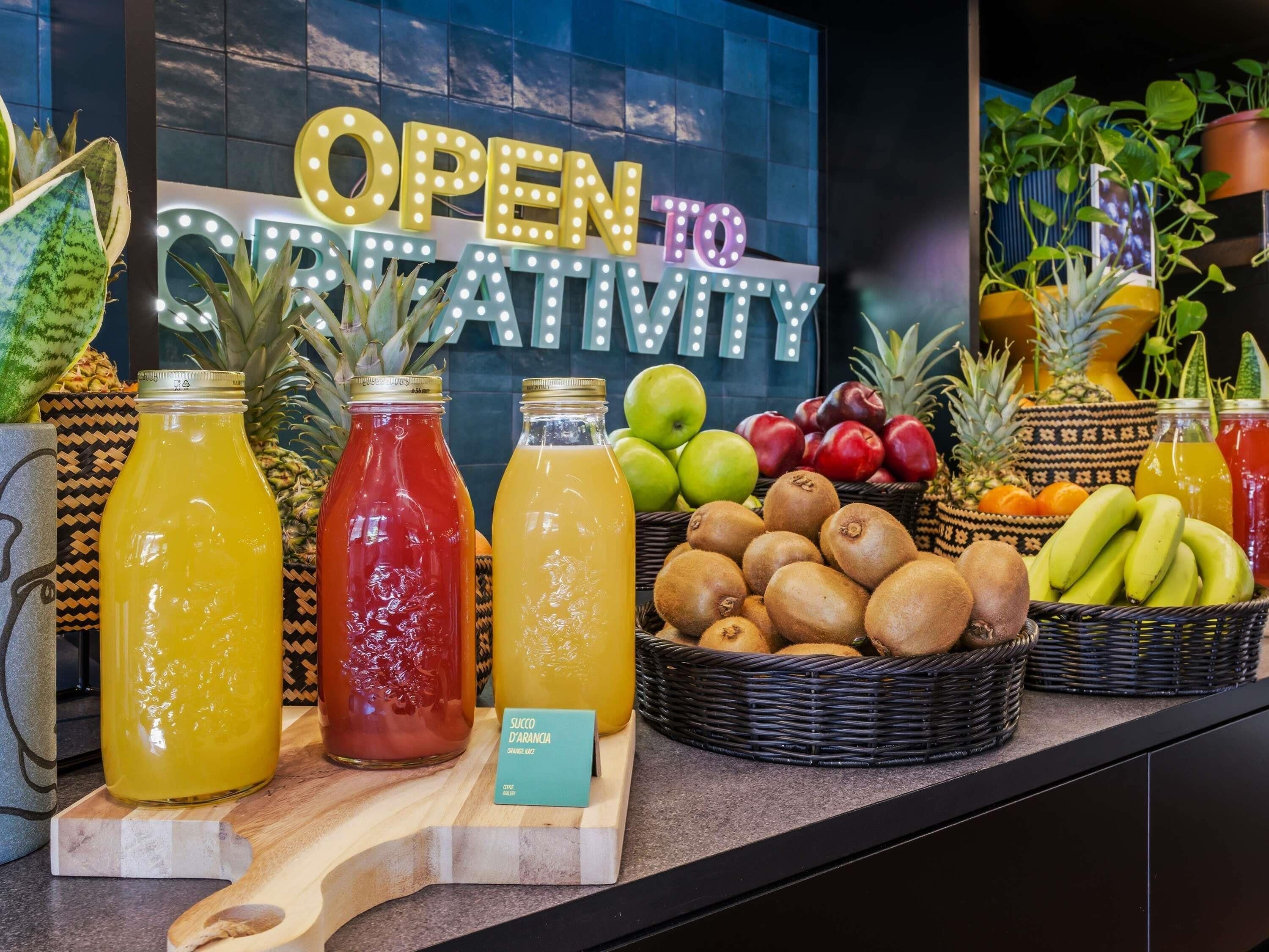 A display of various fruit juices and fresh produce, with a sign reading 'OPEN TO CREATIVITY' in the background.