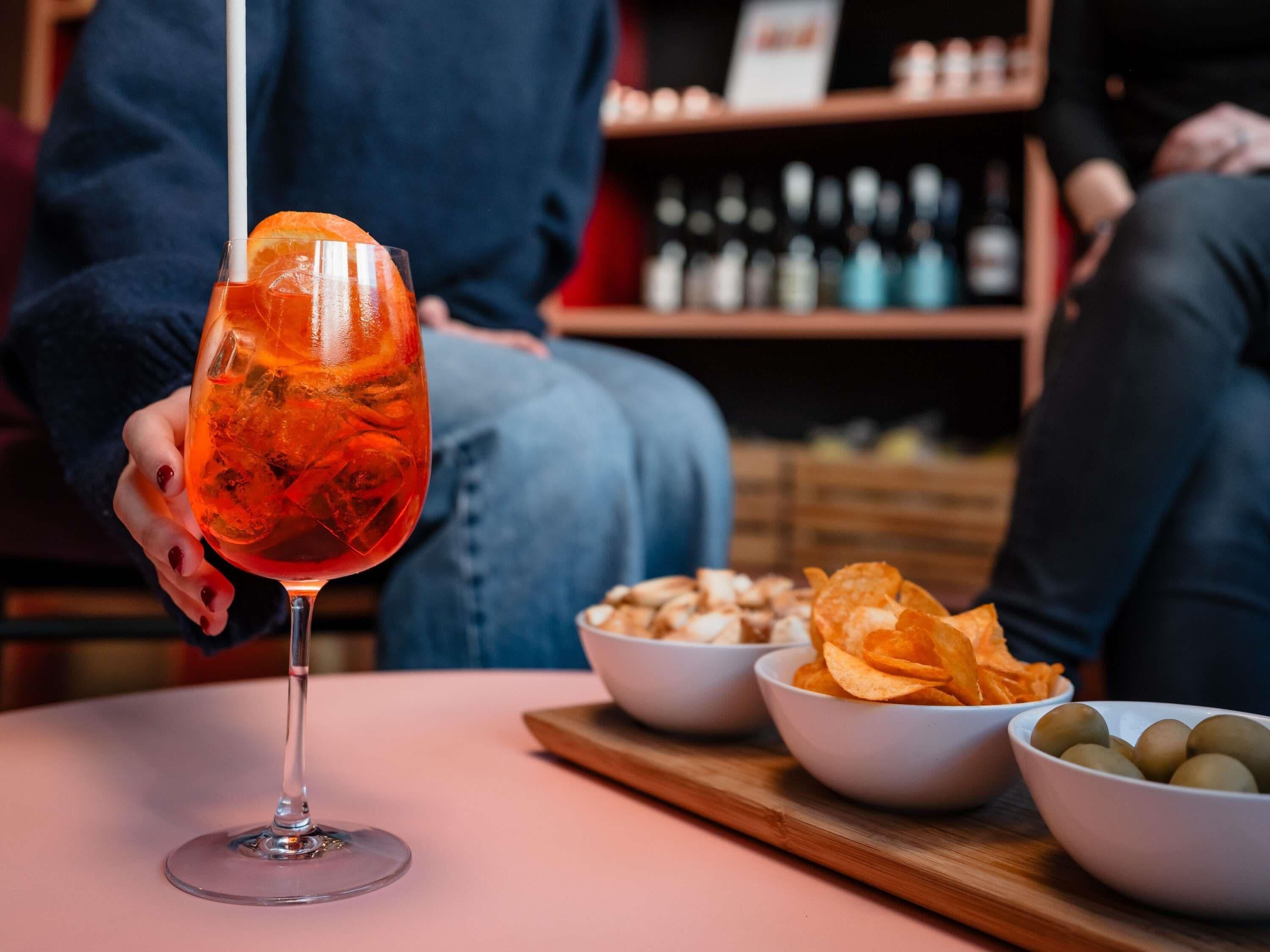 Um copo de cocktail com gelo e uma fatia de laranja sobre uma mesa rosa.