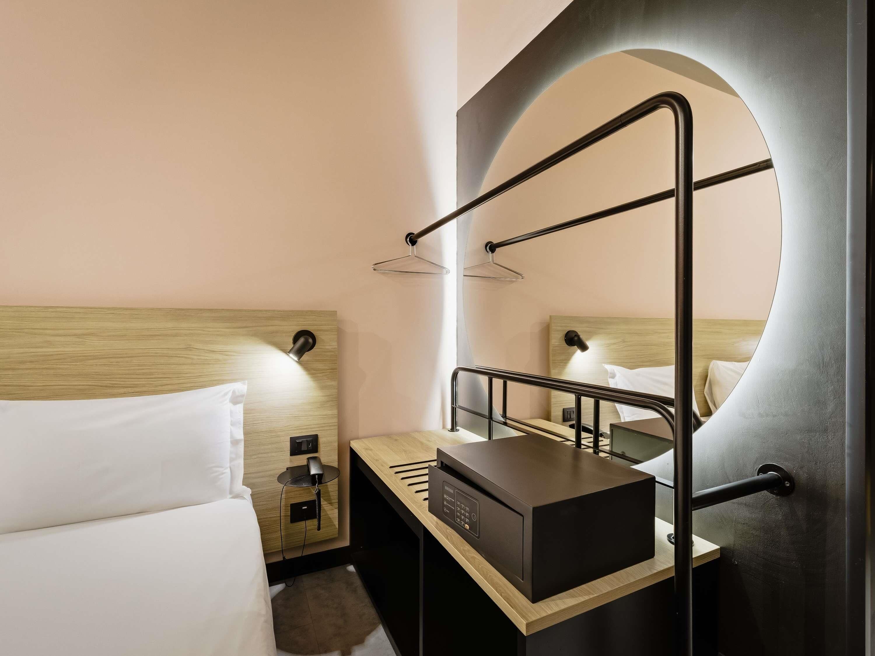 Een hotelkamer met een bed, nachtkastje en een ingebouwd bureau met een computer.