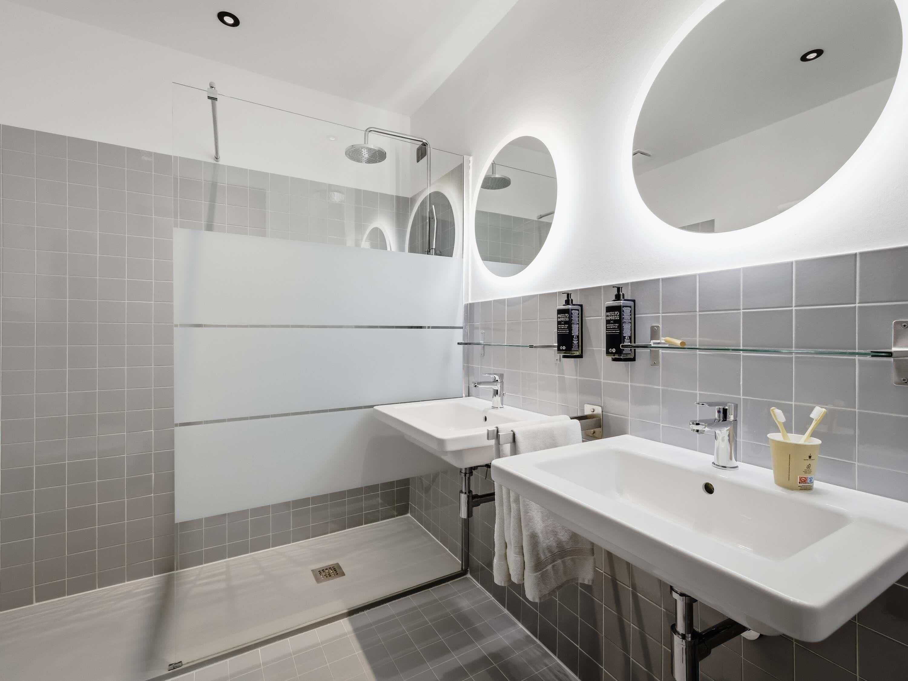 A modern bathroom with two sinks, a glass shower enclosure, and two wall-mounted mirrors.