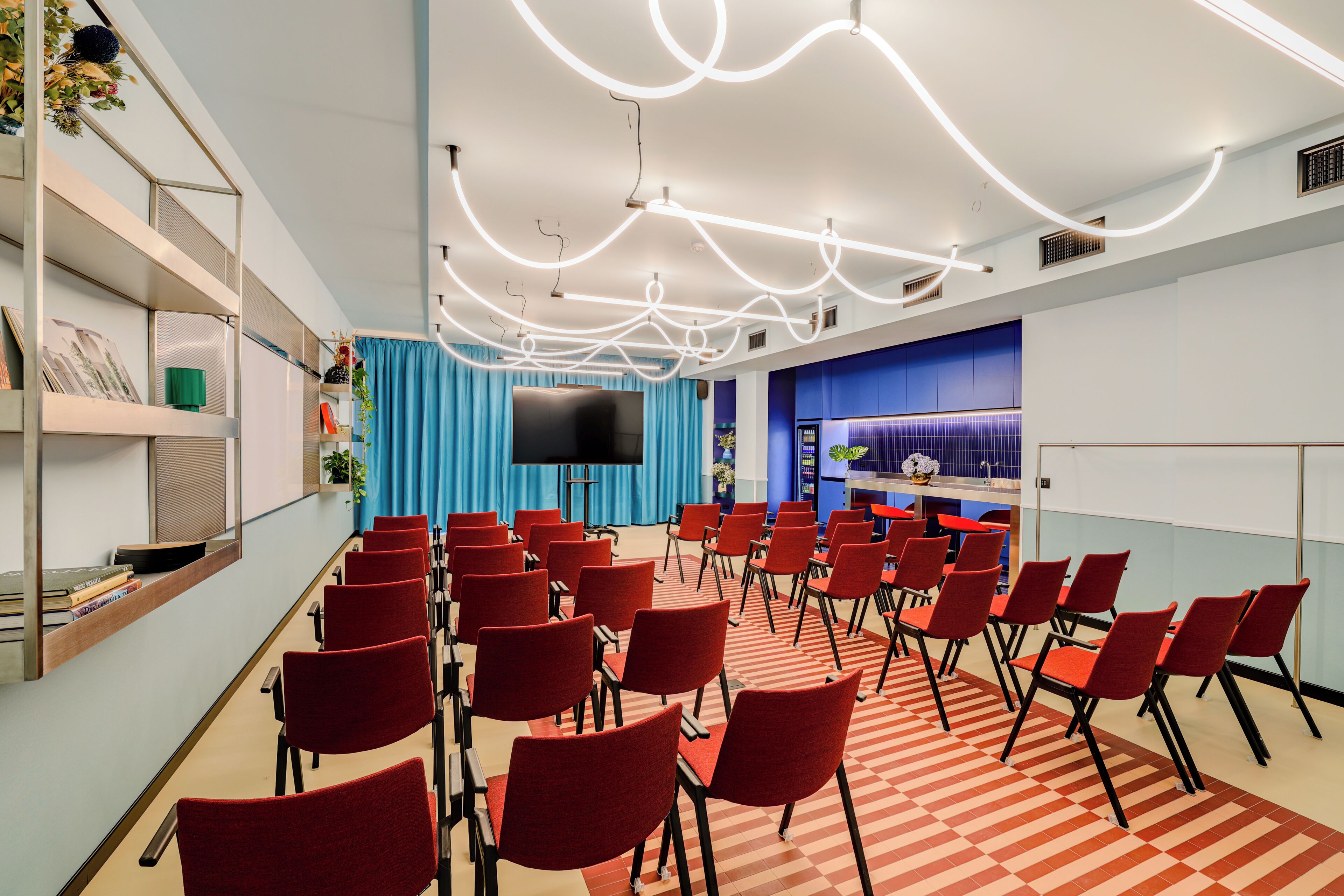 Ett konferensrum med röda stolar, en stor skärm och en blå bakgrundsridå.