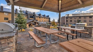 An outdoor patio with picnic tables and grills, surrounded by buildings with a stone facade and a clear sky. - Hilton Vacation Club Cedar Breaks Brian Head (Brian Head)