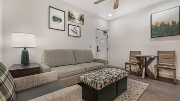 A living room with a sofa, ottoman, side table, lamp, and a ceiling fan.