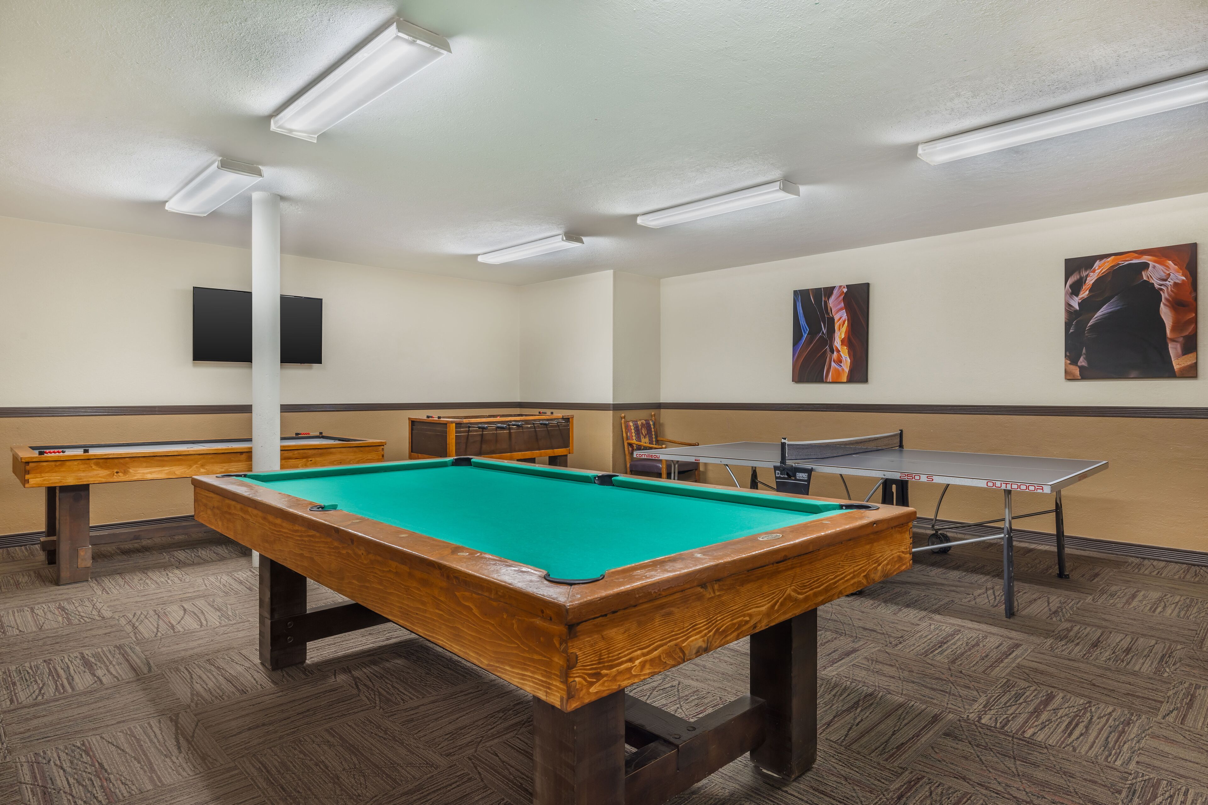 A pool table with a green felt surface, a ping pong table, and a billiards table in a room with wooden flooring and white walls.