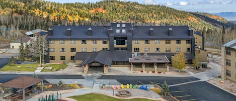 A hotel with a playground, parking, and a view of a forested mountain.