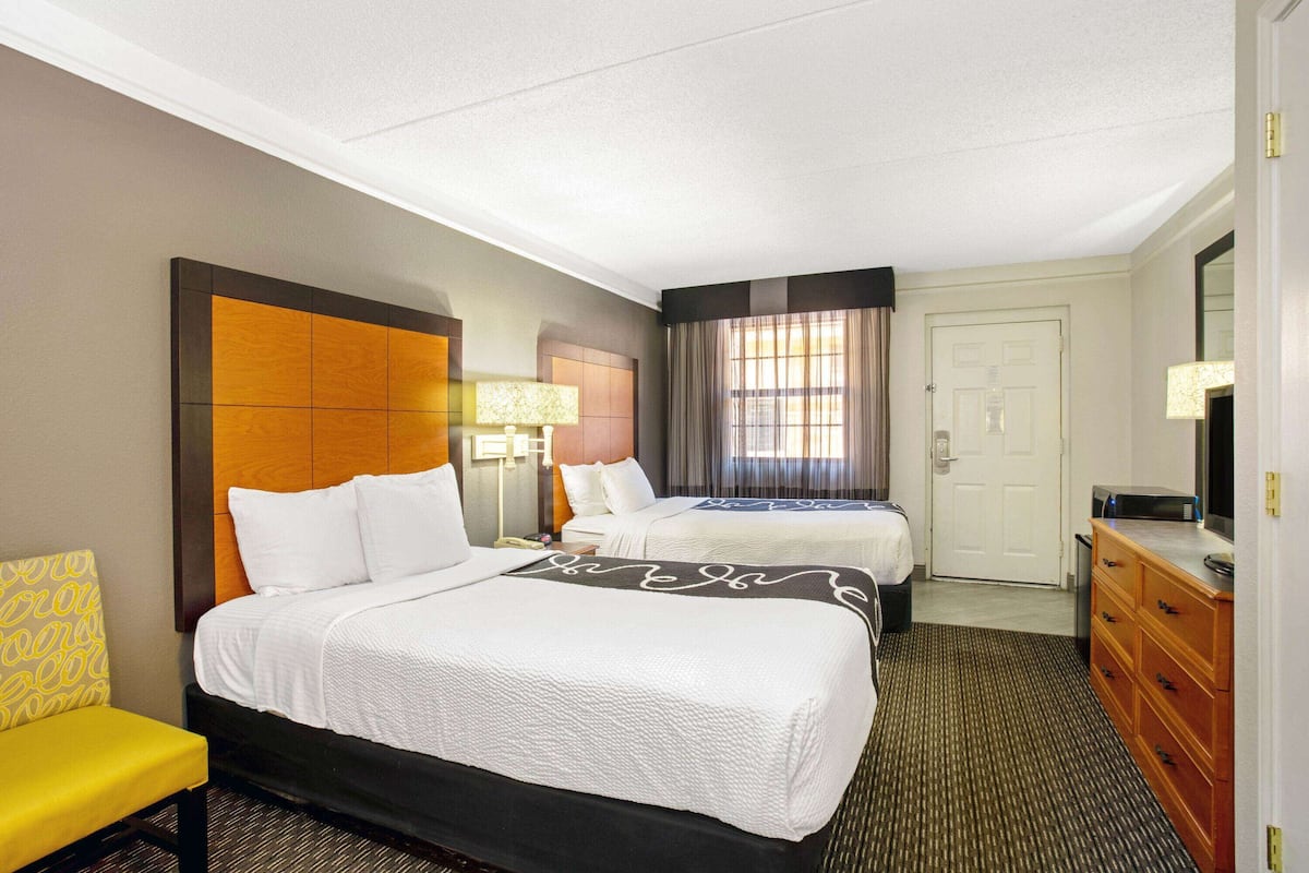 A hotel room with two beds, a desk, a chair, a dresser, and a door.