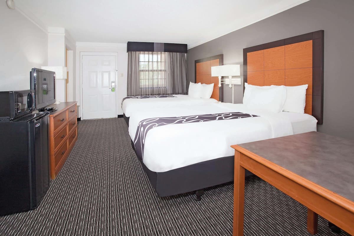 A hotel room with two beds, a desk, a TV, and a dresser.