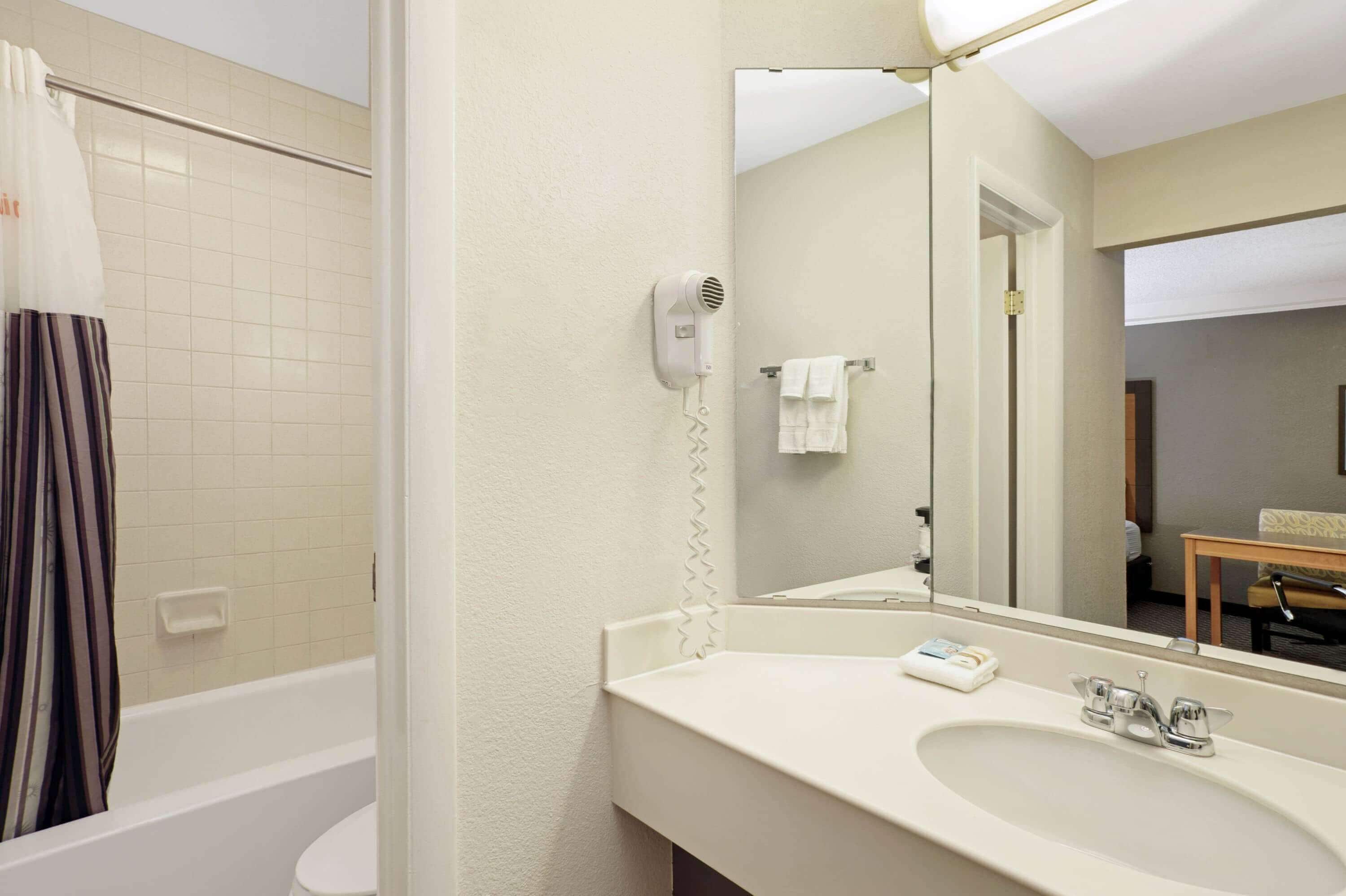 Un baño con bañera, lavamanos, espejo y secador de pelo.
