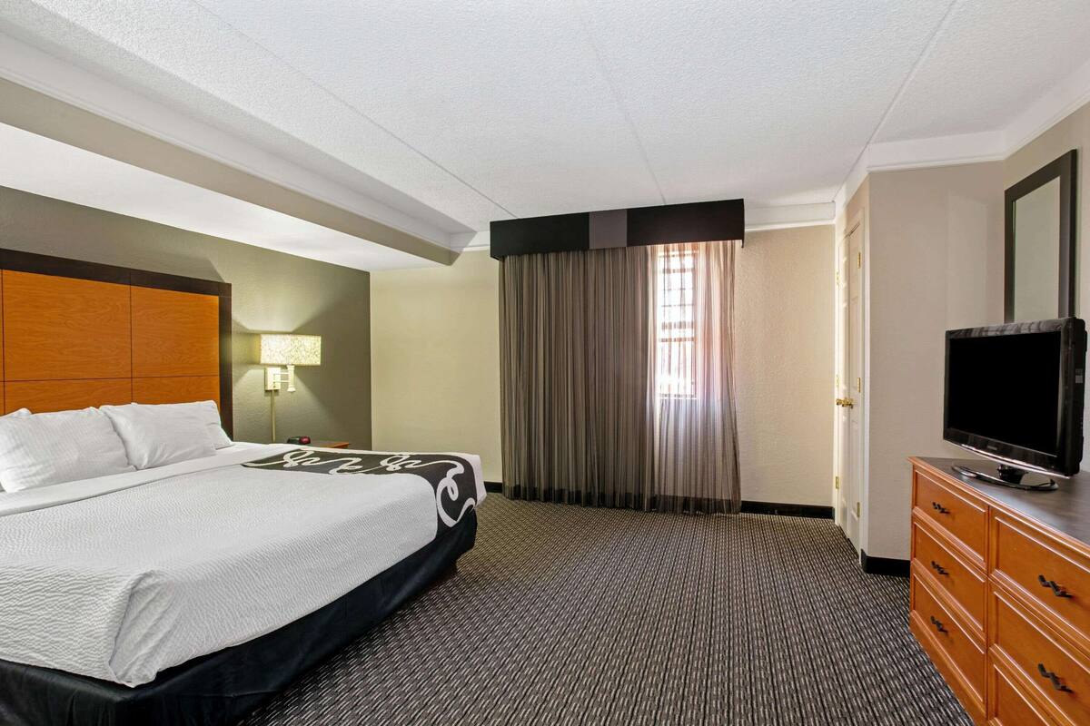 A hotel room with a bed, a television on a dresser, a lamp, and a window with curtains.