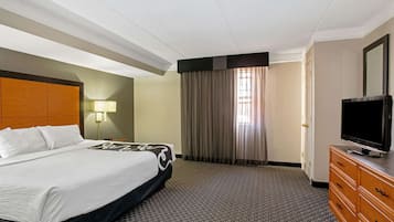 Habitación de hotel con cama, televisor en una cómoda, lámpara y ventana con cortinas.