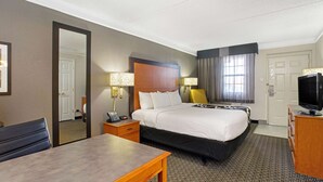 A hotel room with a large bed, a desk, a chair, a television, and a mirror. - Travelodge by Wyndham Golden/Denver (Wheat Ridge)