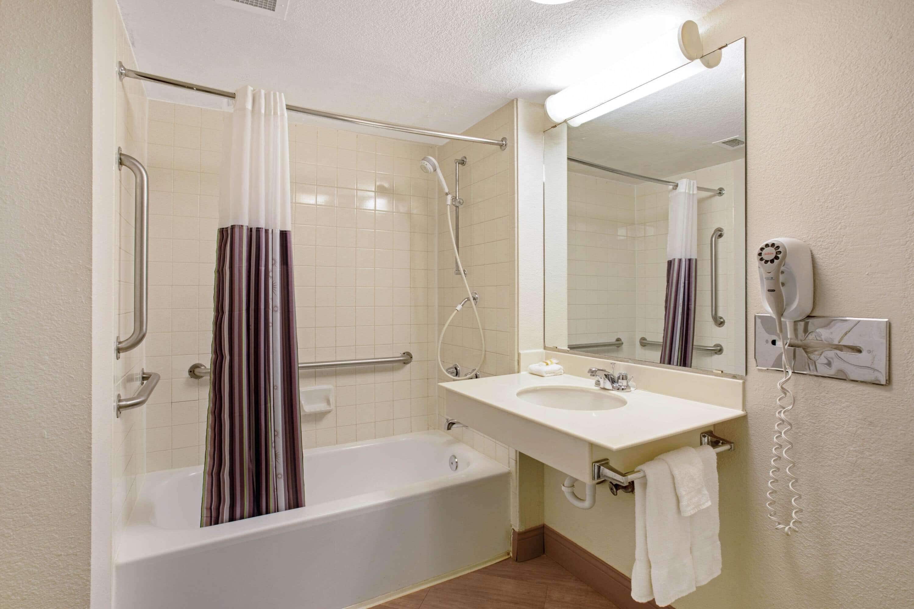 A bathroom with a bathtub, a shower, a sink, a mirror, and a hairdryer.