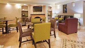 A dining area with a fireplace, a television mounted above it, and a sofa with cushions. - Travelodge by Wyndham Golden/Denver (Wheat Ridge)