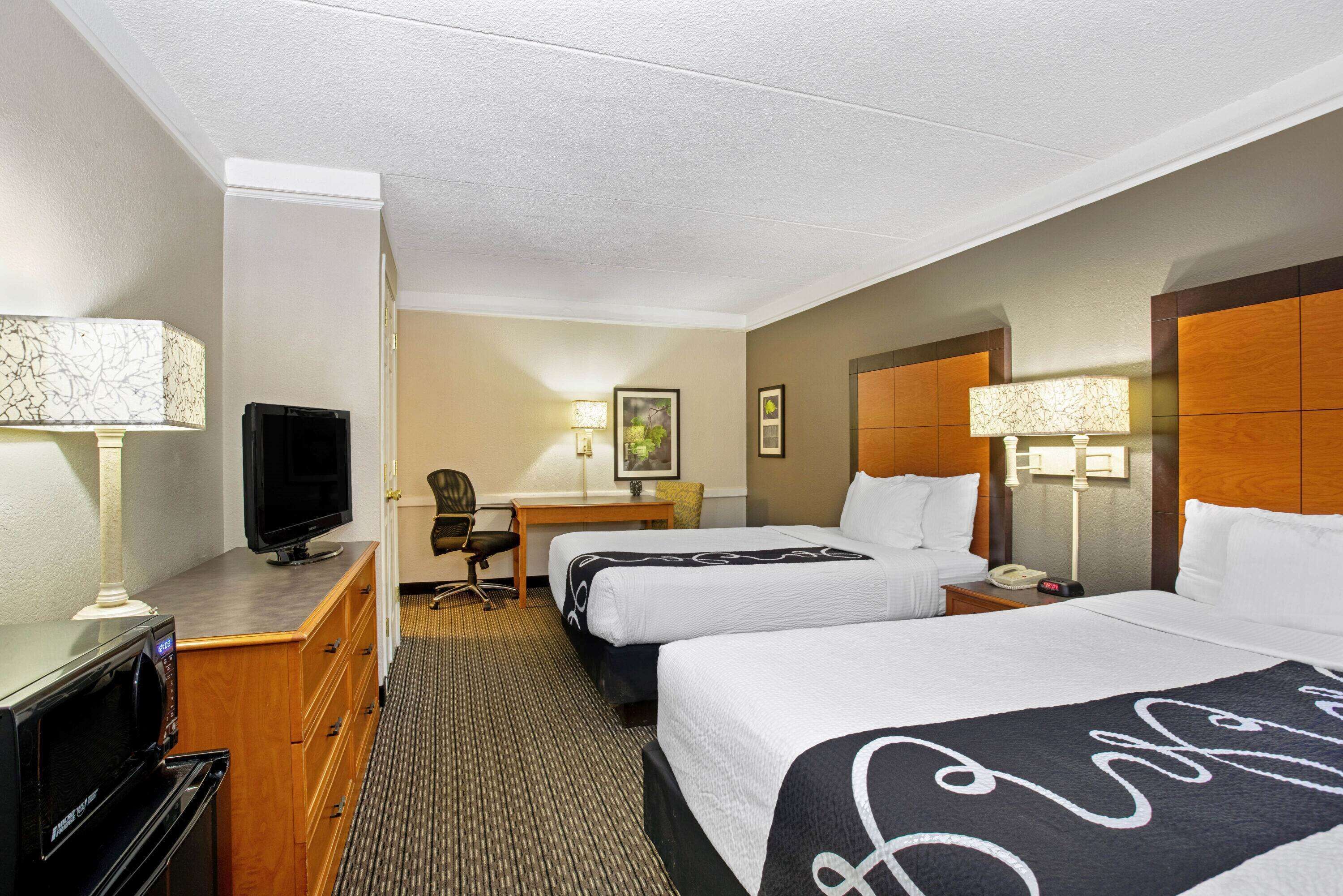A hotel room with two beds, a desk, a television, a microwave, and a lamp.