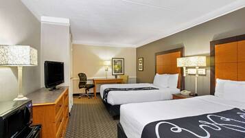 A hotel room with two beds, a desk, a television, a microwave, and a lamp.