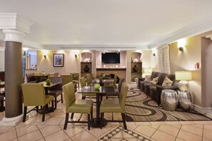 A hotel lobby with a dining area, a sofa, and a flat-screen TV.