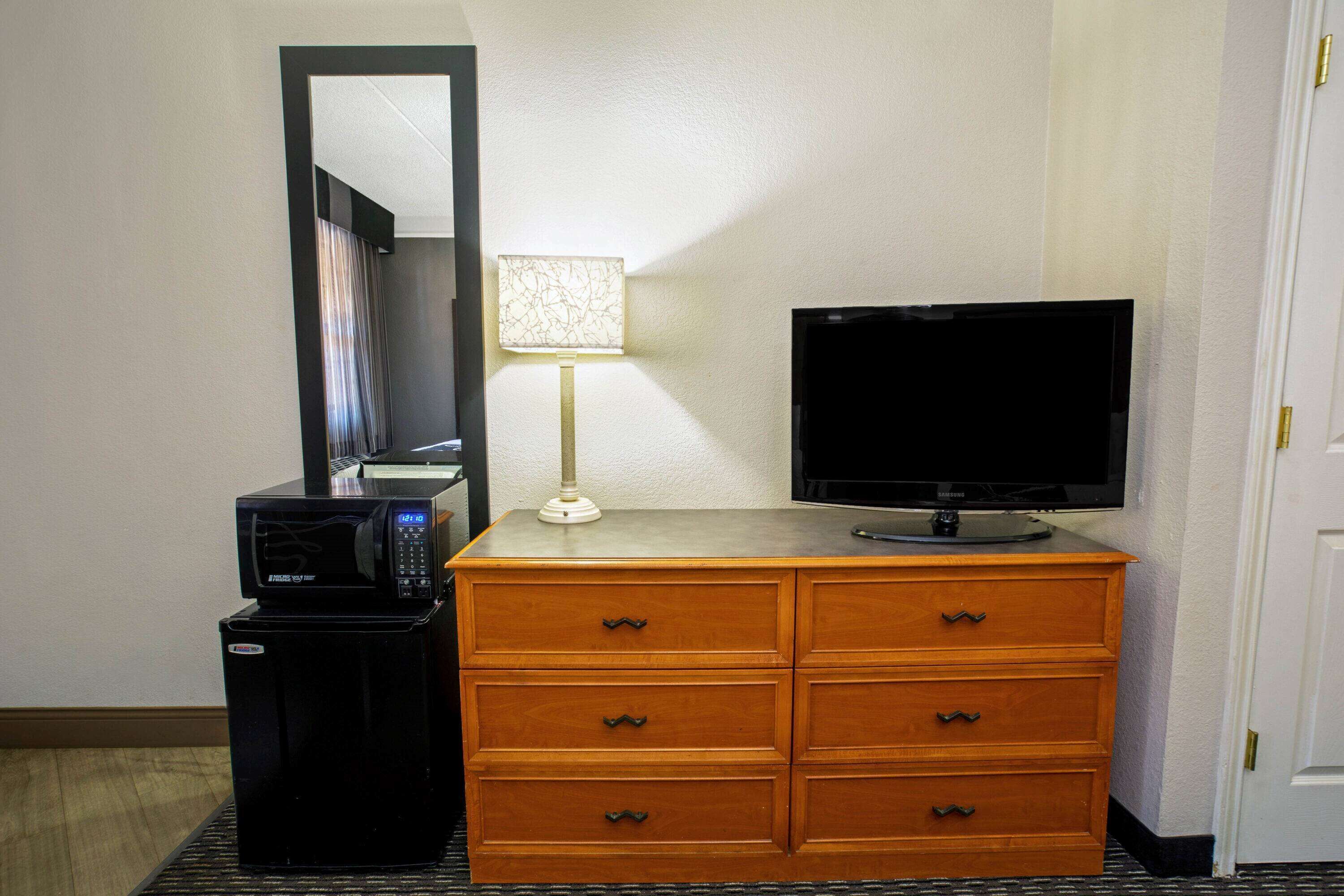 Una habitación de hotel con un aparador de madera, un televisor, un microondas y una lámpara.