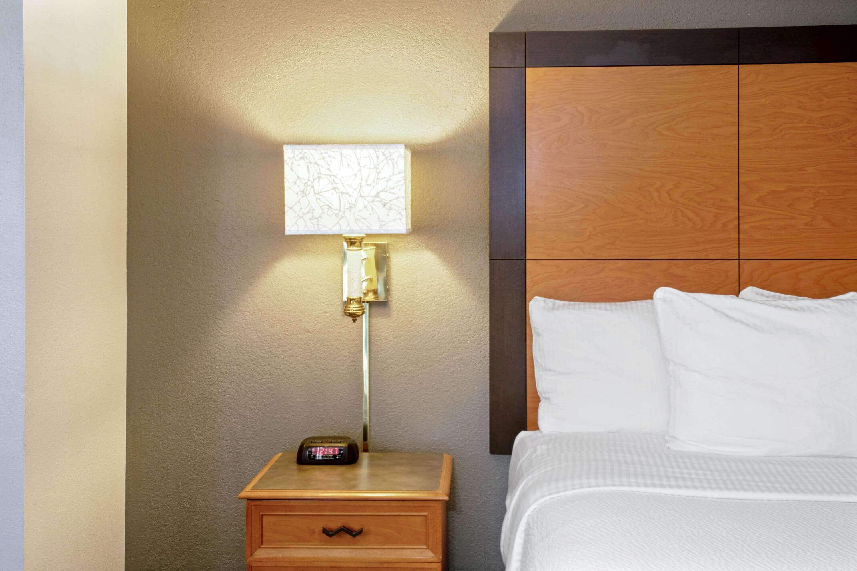 A hotel room with a wooden headboard, a bedside table with a lamp, and a bed with white bedding.