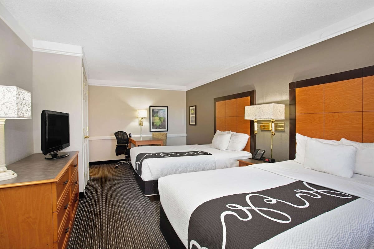 A hotel room with two beds, a TV, a desk with a lamp, and a chair.