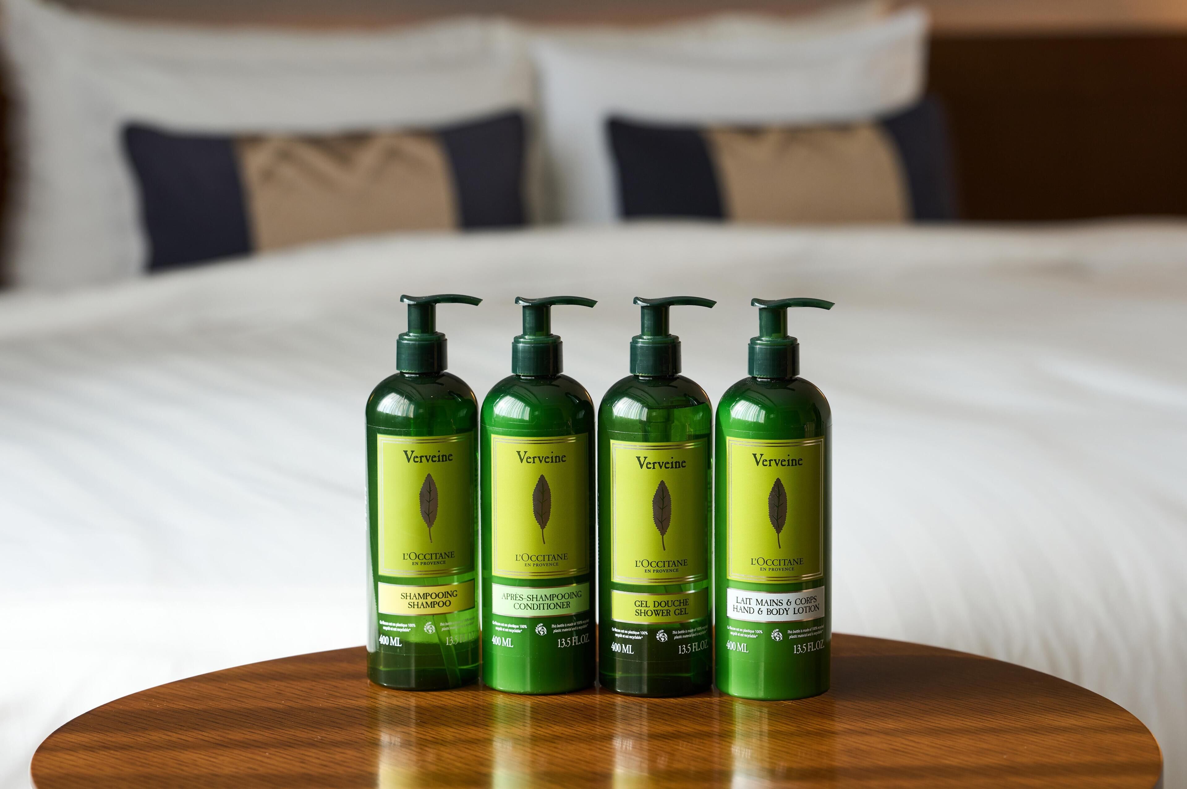 Quatre bouteilles vertes de liqueur à la verveine, posées sur une table en bois dans une chambre d’hôtel.