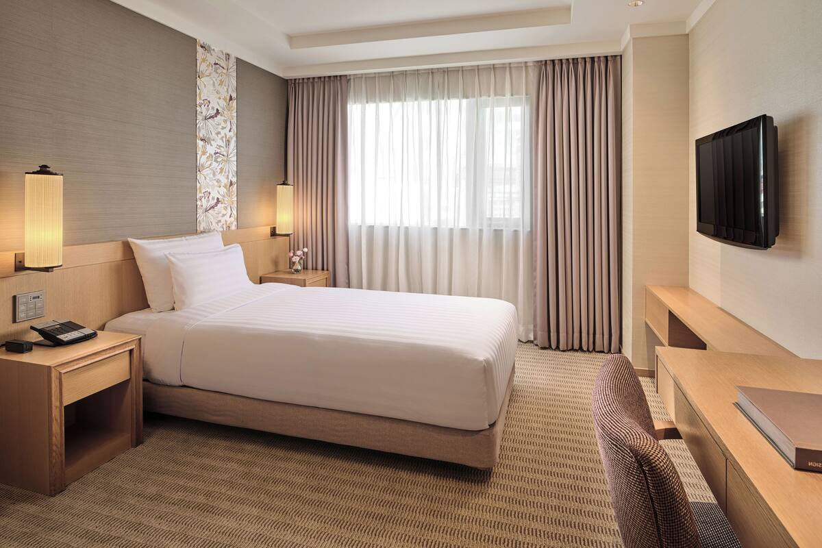Quarto de hotel com uma cama grande, mesas de cabeceira, uma televisão de tela plana e uma escrivaninha com cadeira.