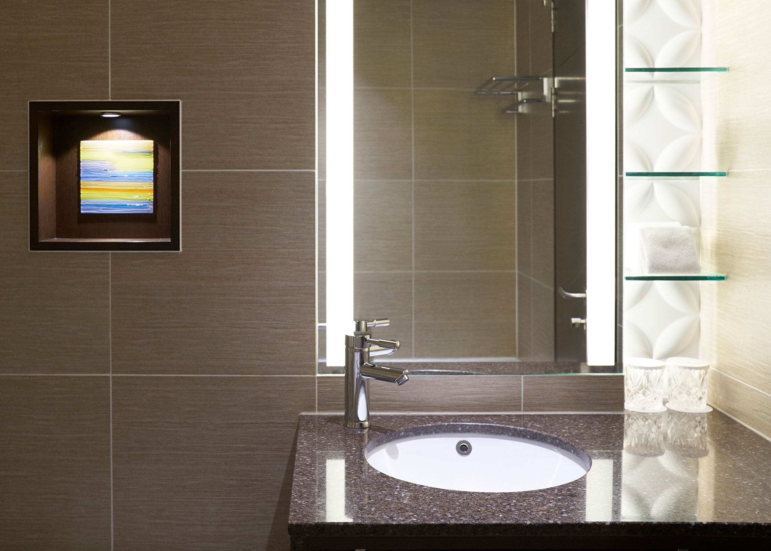 A bathroom with a granite countertop sink, a mirror, and a framed artwork.