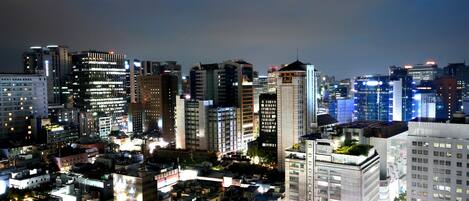 Un paisaje urbano nocturno con rascacielos, ventanas iluminadas y un ambiente citadino denso.
