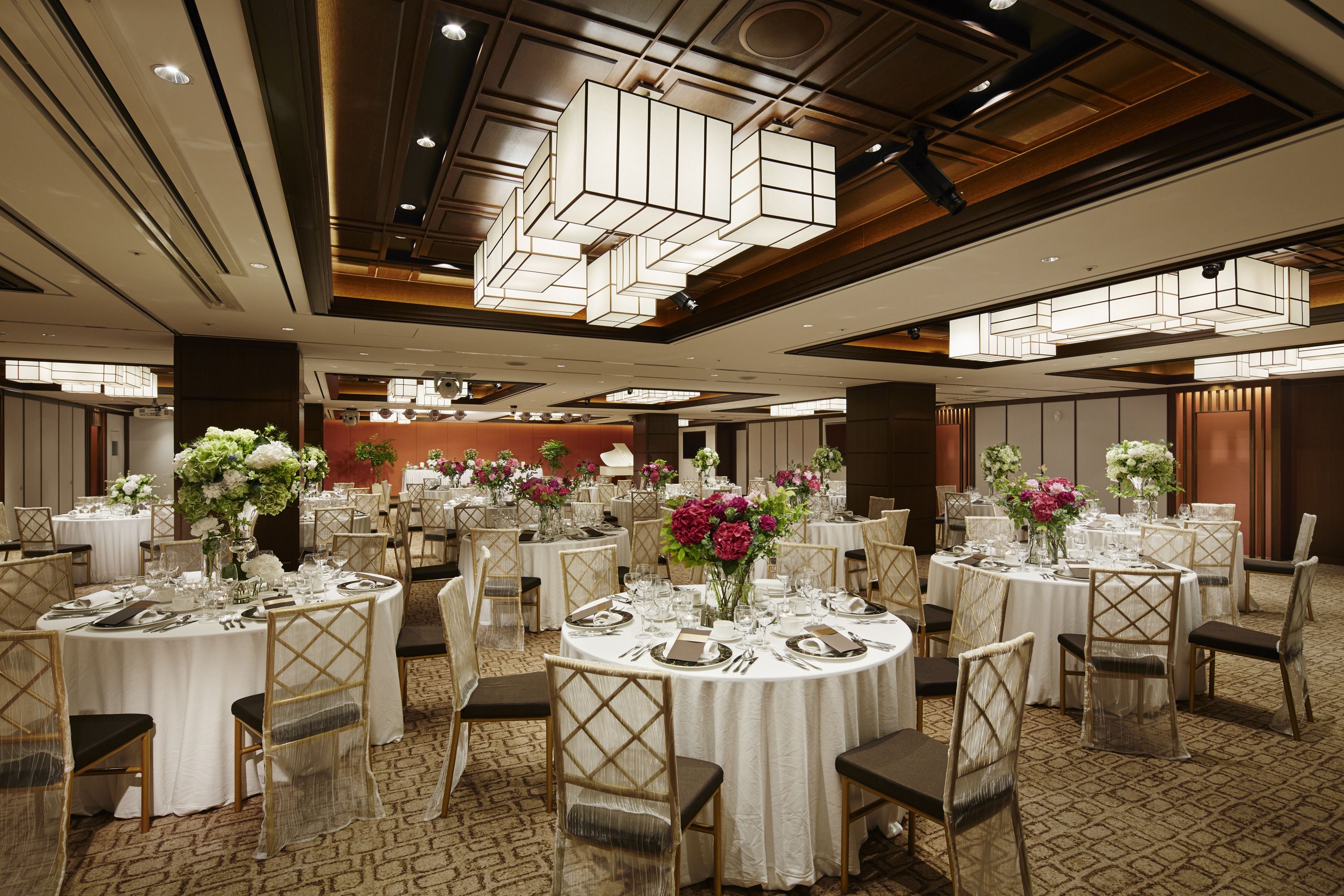 A banquet hall with round tables set for dining, featuring white tablecloths, chairs, and floral centerpieces.
