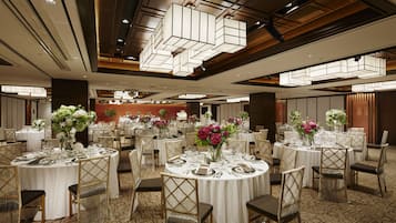 A banquet hall with round tables set for dining, featuring white tablecloths, chairs, and floral centerpieces.