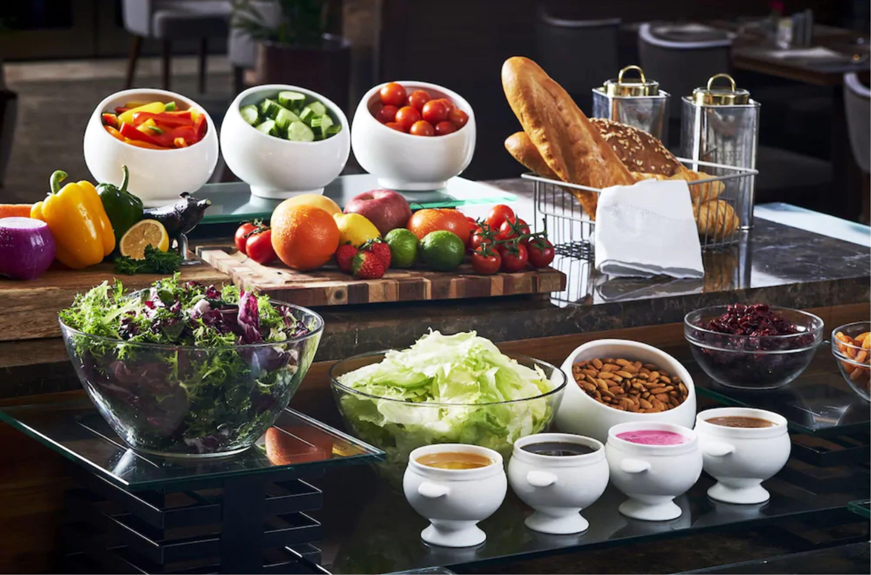 A buffet table with various food items including salads, fruits, vegetables, bread, and condiments.